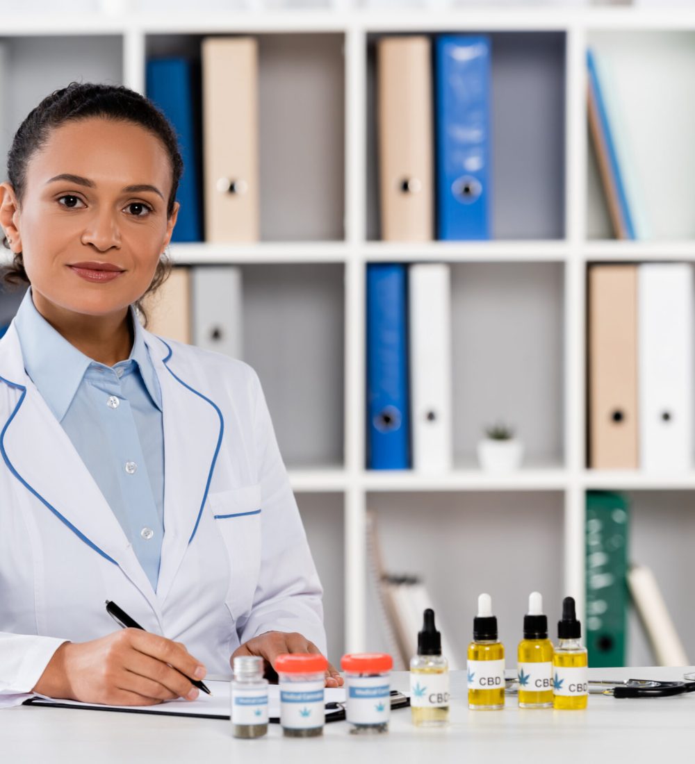african american doctor writing prescription on clipboard near bottles with legal cbd and medical